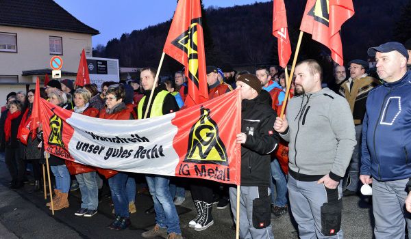 Personen stehen mit Fahnen der IG-Metall auf der Straße und demonstrieren. Die vordere Reihe hält ein Banner mit der Aufschrift: Warnstreik ist unser gutes Recht. Es dämmert.