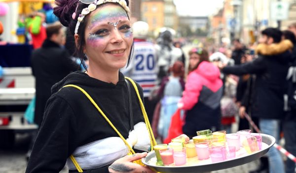 Eine bunt geschminkte Frau hält ein Tablett mit Schnappsgläßern.