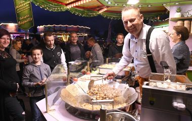 Ein Mann steht in einem Verkaufsstand mit Essen. Davor stehen Kunden.