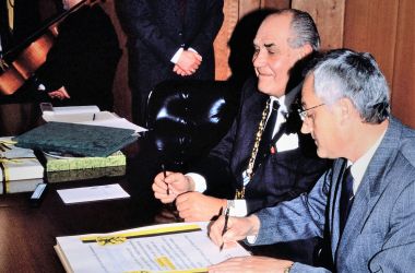 Zwei Männer setzen ihre Unterschrift unter eine Urkunde, die die Städtepartnerschaft besiegeln.