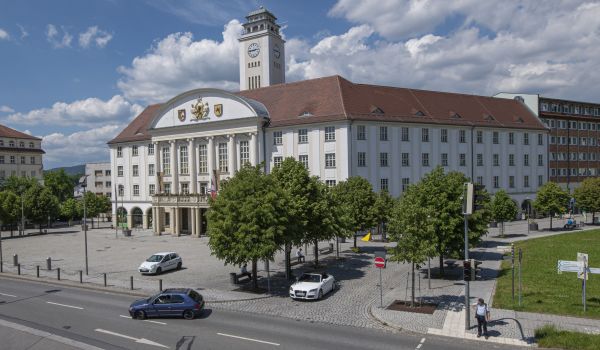 EIn weißes Gebäude mit rotem Dach und einem Turm. Es ist das Rathaus der Stadt Sonneberg. Die Sonne scheint.