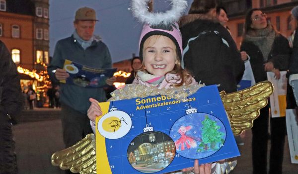 Ein Kind im Engelskostüm hält einen Sonneberger Adventskalender in der Hand.