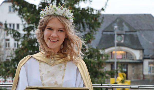 Eine Frau ist als Christkind gekleidet. Im Hintergrund ist der Bahnhof der Stadt Sonneberg.