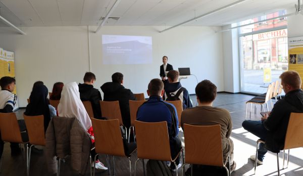 Schüler sitzen im Halbkreis und hören einem Referenten zu.