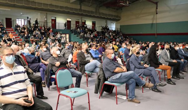 In einer Turnhalle sitzen Menschen in Stuhlreihen.