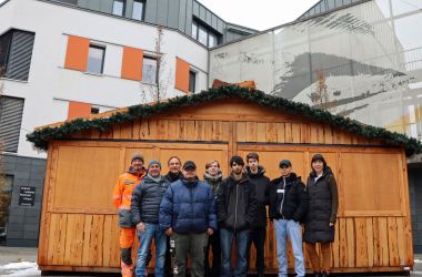 Mehrere Personen stehen vor einer großen Weihnachtsmarkthütte aus Holz.