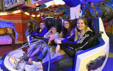 Vier Menschen sitzen in einem Fahrgeschäft.