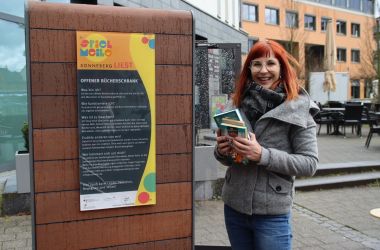 Frau mit Büchern vor dem Bücherschrank.