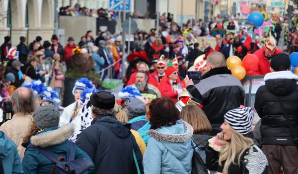 Kostümierte Kinder und Erwachsene stehen an der Straße und beobachten den Umzug.