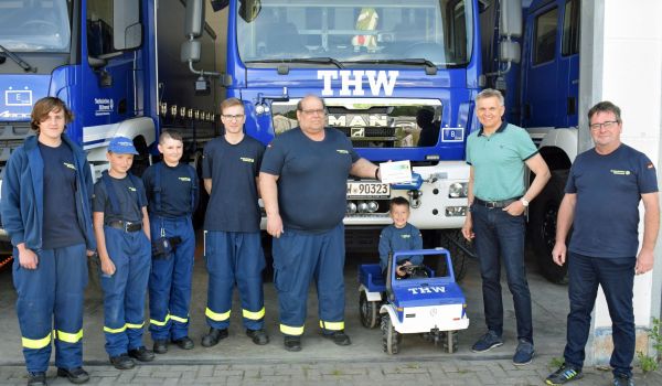 Mehrere Personen stehen vor einer Garage mit THW-Fahrzeugen.