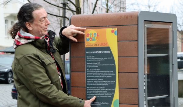 Ein Mitarbeiter montiert ein Schild an einem Bücherschrank.
