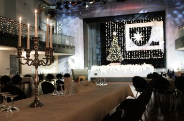 Lange gedeckte Tische stehen in einem großen Saal. Im Hintergrund ist eine weihnachtlich geschmückte Bühne.