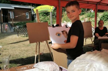 Ein Junge steht vor einer Staffelei malt ein Gesicht.