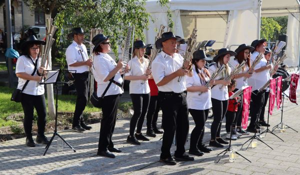 Mehrere Personen stehen in drei Reihen hintereinander. Sie halten Blechblasinstrumente in den Händen und spielen darauf.