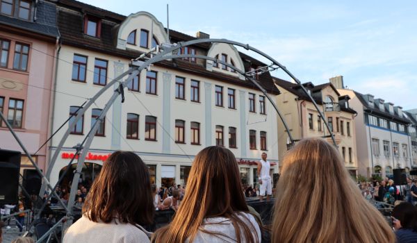 Viele Menschen stehen in der Innenstadt. In der Mitte eine große Turn-Konstruktion aus Metall.