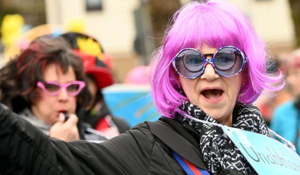 Eine Frau trägt zwei Brillen und eine lilafarbene Perücke.