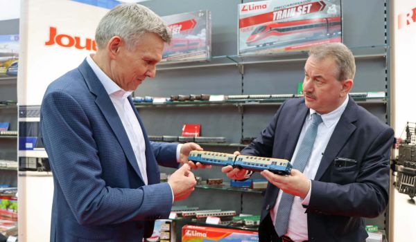 Zwei Männer stehen nebeneinander und halten eine Modellbahn in den Händen.