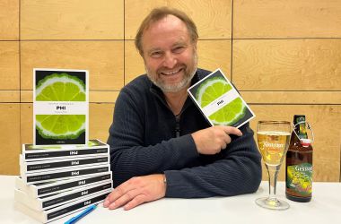 Ein Mann sitzt an einem Tisch und hält ein Buch in der Hand.