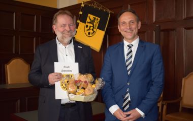 Zwei Männer stehen nebeneinander. Der Mann links hält ein Präsent und eine Urkunde in den Händen.