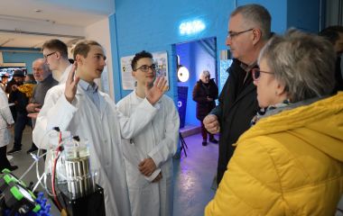 Zwei Jugendliche in weißen Kitteln erklären Experimente für Interessierte.