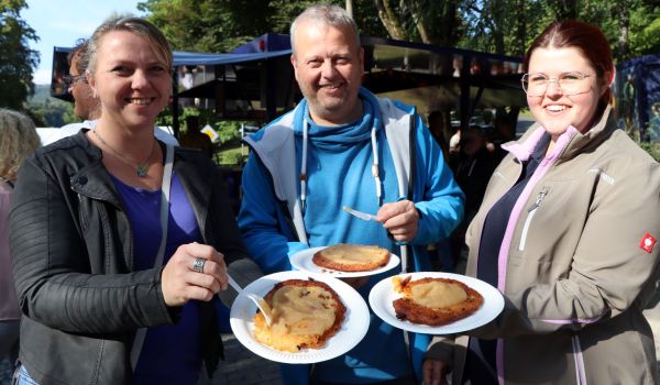 Drei Personen halten einen Pappteller in den Händen. Auf den Tellern ist Kartoffelpuffer mit Apfelmus.