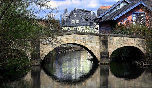 Eine Brücke aus hellem Sandstein die über einen Fluss führt. Im Hintergrund stehen Häuser.