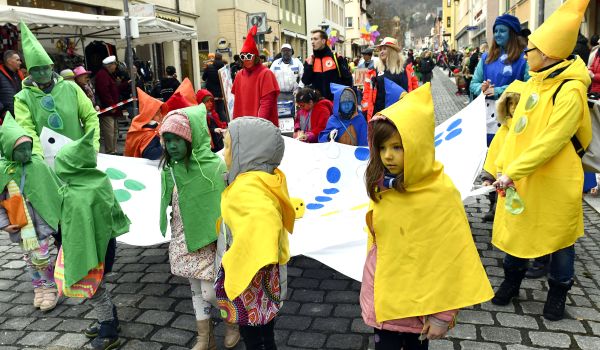 Kinder und Erwachsene sind als Mensch-ärgere-dich-nicht-Figuren gekleidet und tragen ein zugehöriges Spielbrett.