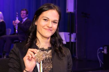 Eine junge Fau hält eine schneeflockenförmige Medaille in der Hand.