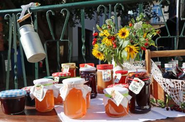 Auf einem Tisch steht selbstgemachter Gelee. Dahinter steht ein Strauß Sonnenblumen.