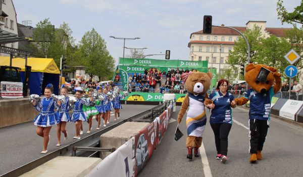 Tanzmariechen und Maskottchen laufen entlang der Rennstrecke.