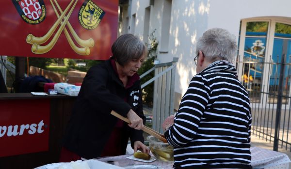 Eine Frau steht hinter einem Tisch und verkauft in Essig eingelegte Gurken an eine Kundin.