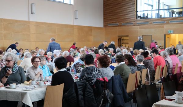 Frauen sitzen an langen gedeckten Tischen.