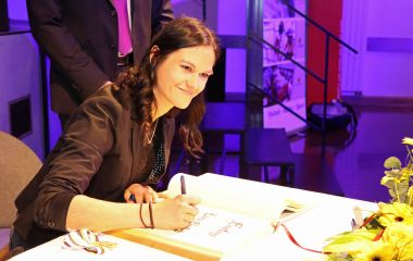 Eine junge Frau sitzt an einem Tisch und schreibt etwas in ein Buch