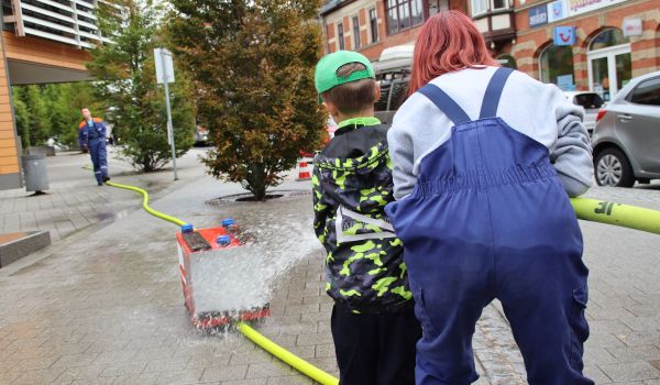 Ein Kind schiebt ein kleines Feuerwehrauto mit dem Strahl eines Feuerwehrschlauches an.