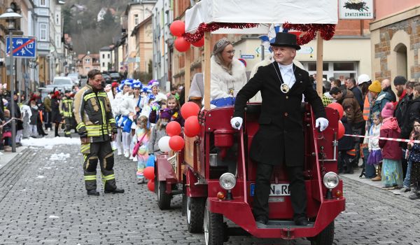 Ein rotes geschmücktes Fahrzeug führt den Umzug an.