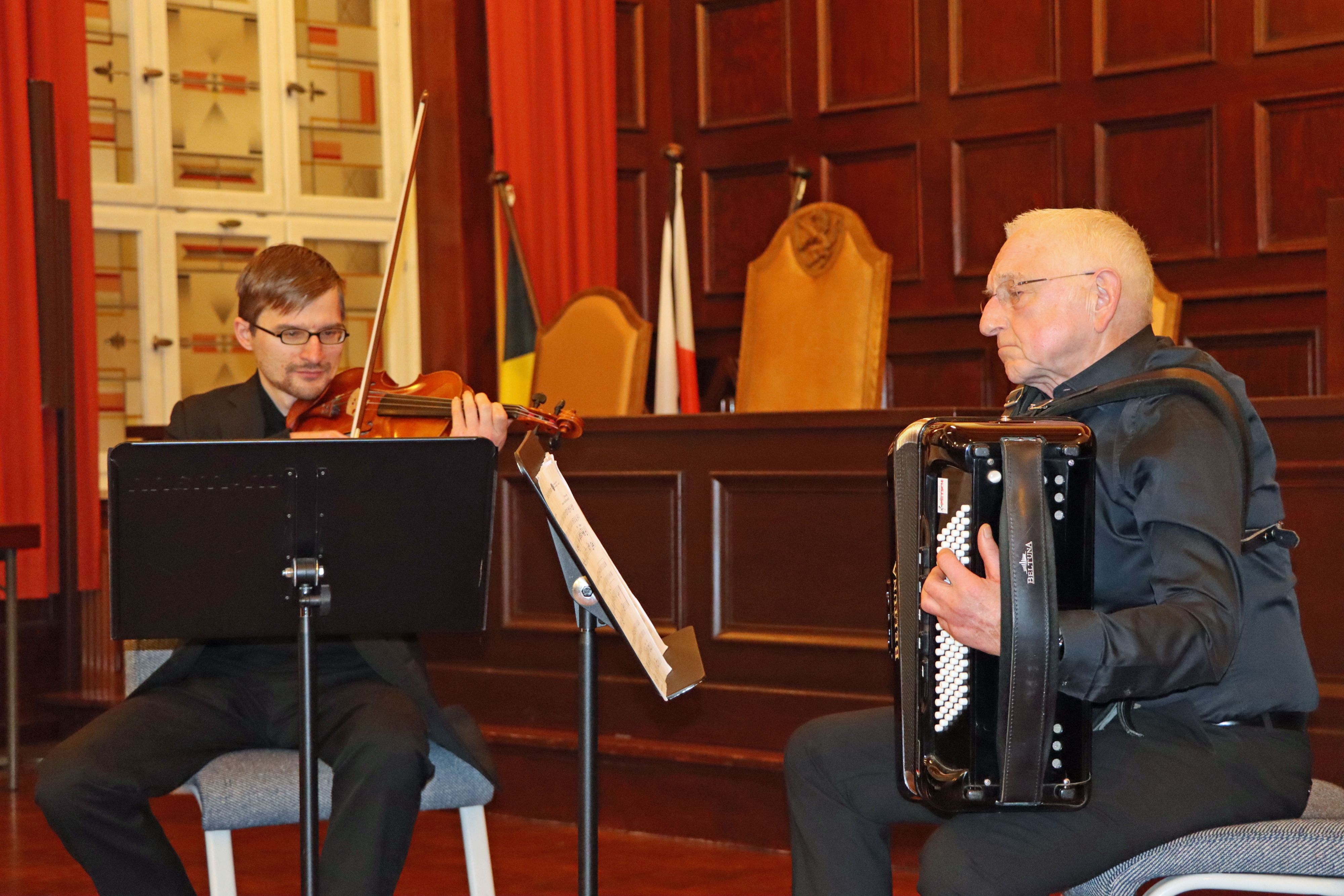 Ein Mann spielt sitzend Akkordeon. Ein weiterer Mann spielt Geige.