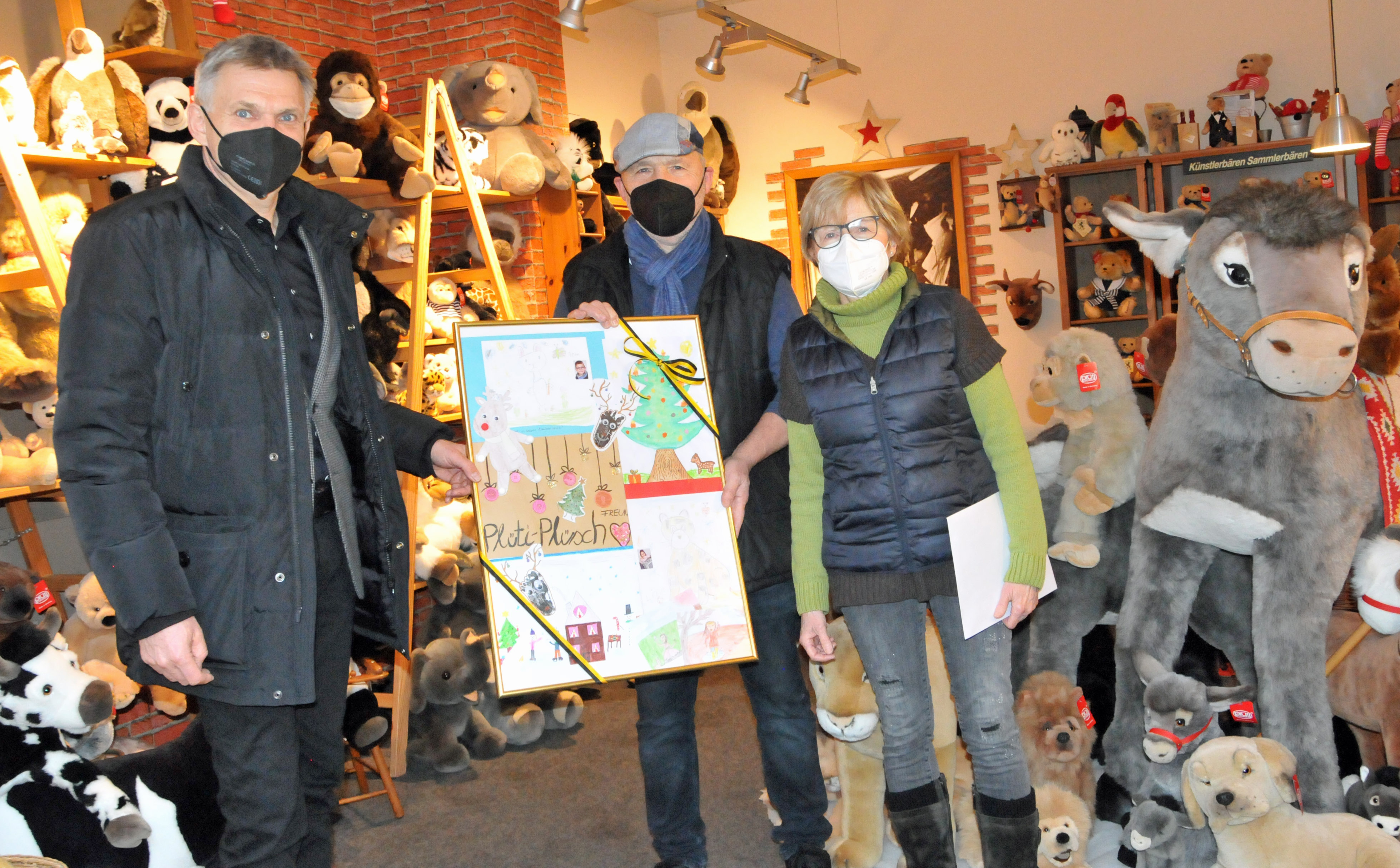 Ein Mann überreicht ein Bilderrahmen mit Kinderzeichnungen an zwei Personen. Sie sind umgeben von verschiedensten Plüschtieren.