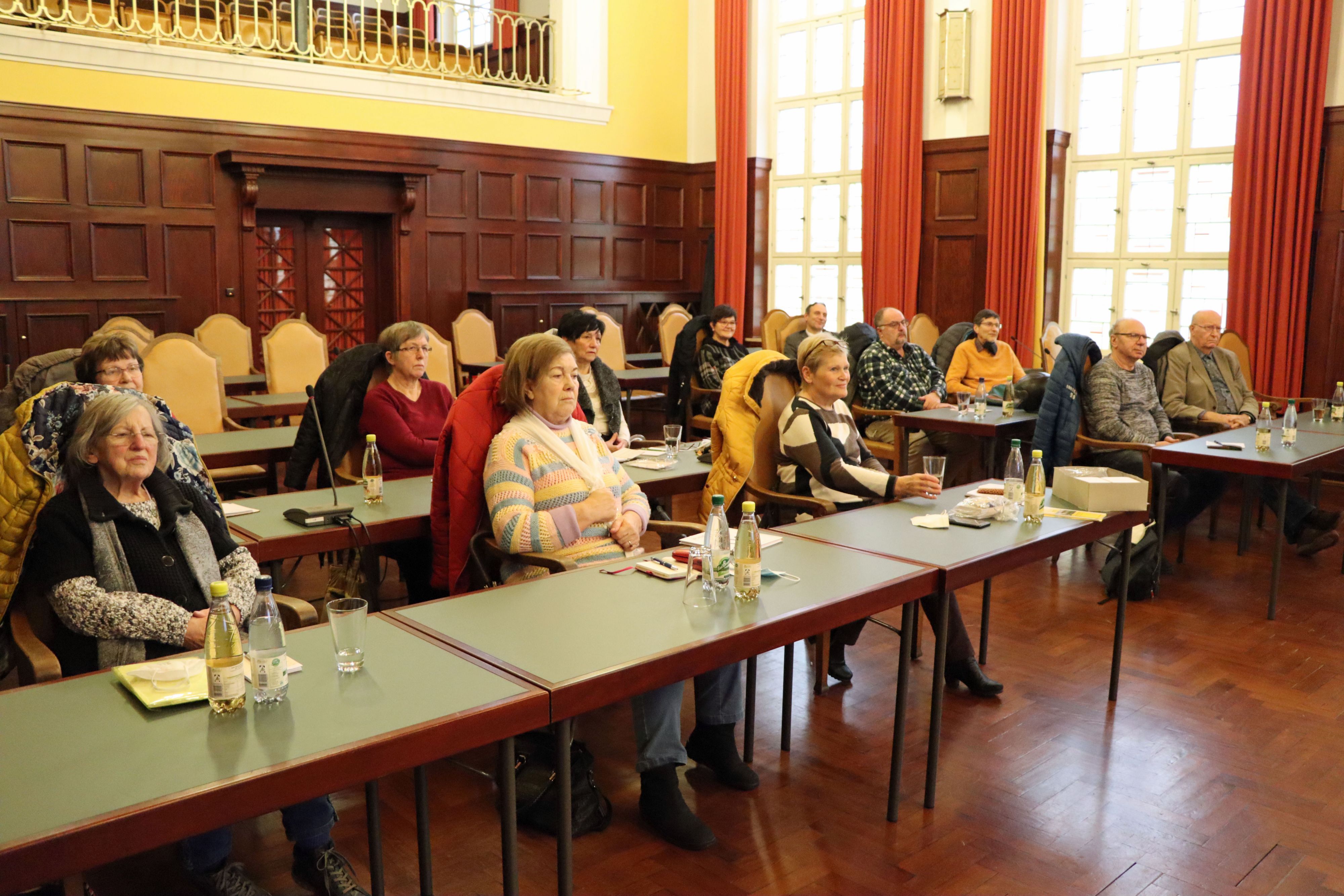 Mehrere Personen sitzen hintereinander in Tischreihen.