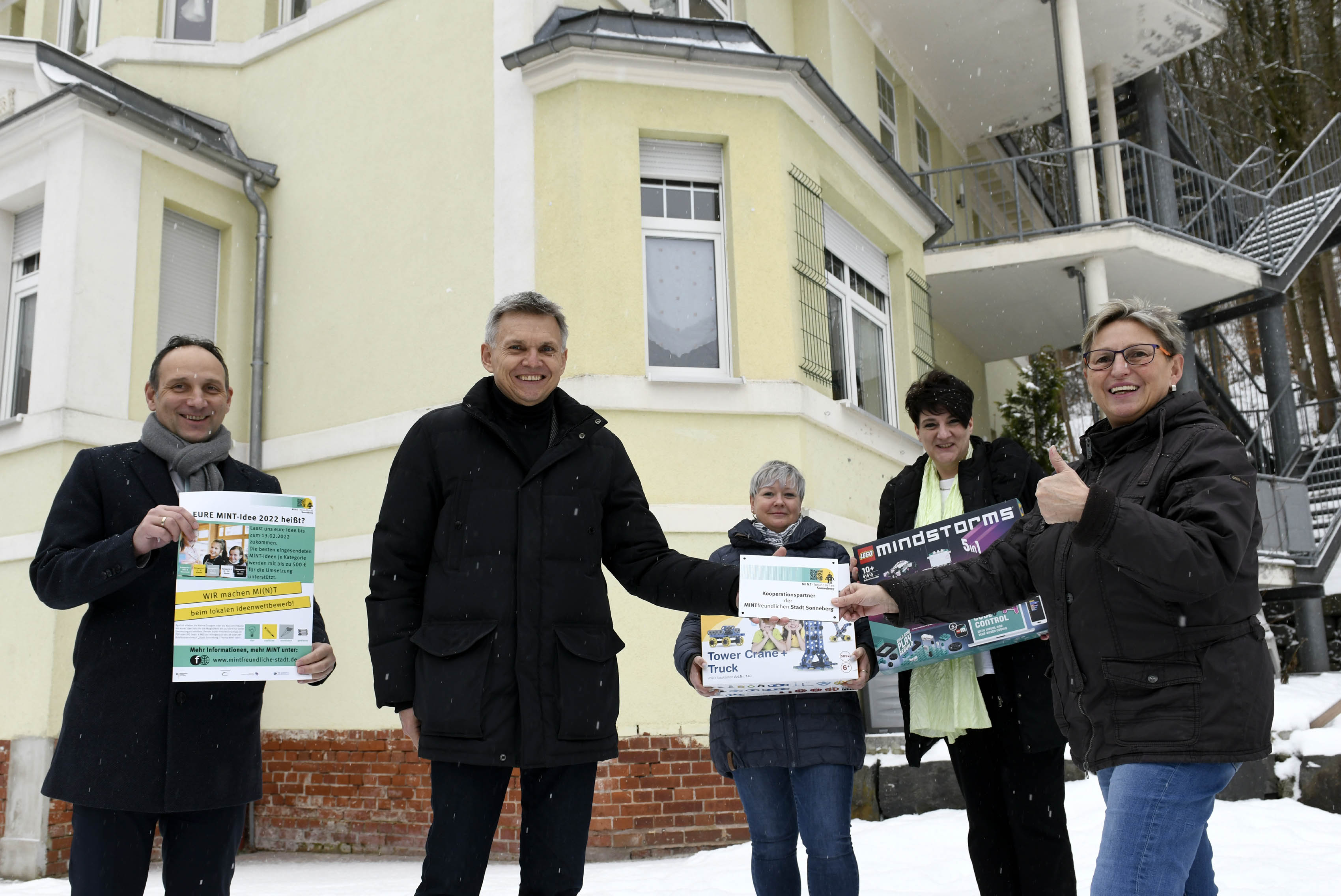 Zwei Männer überreichen eine Plakette für Zusammenarbeit und einige Baukästen an die Einrichtungsleitung.