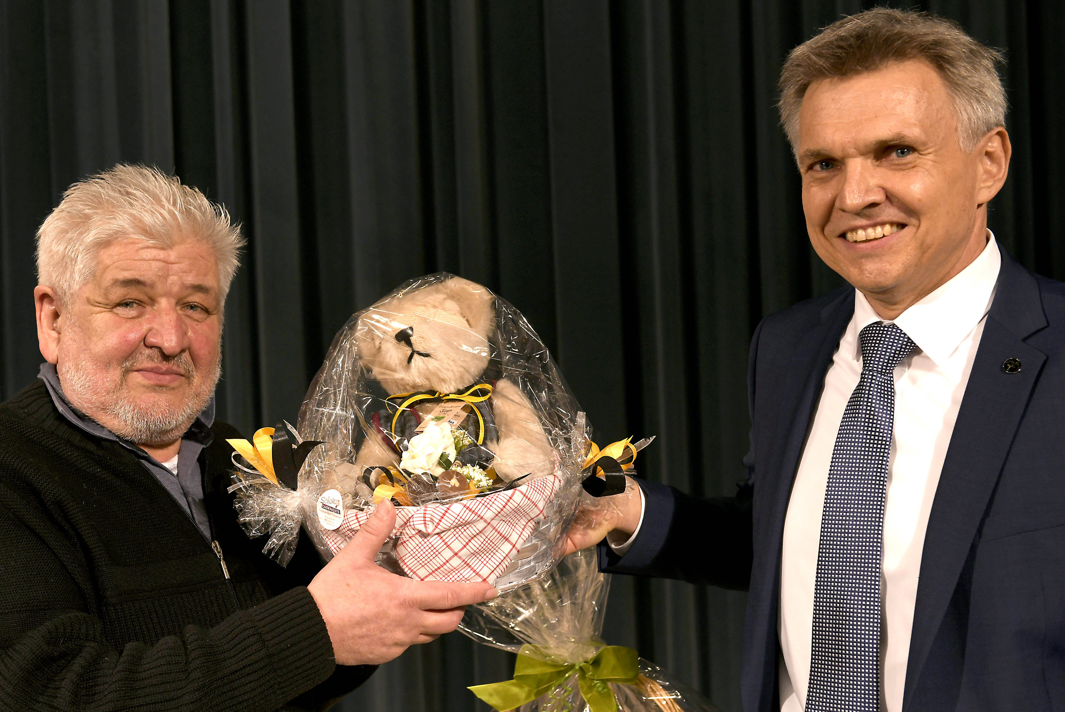 Ein Mann im Anzug überreicht einem anderen Mann einen Presentkorb.