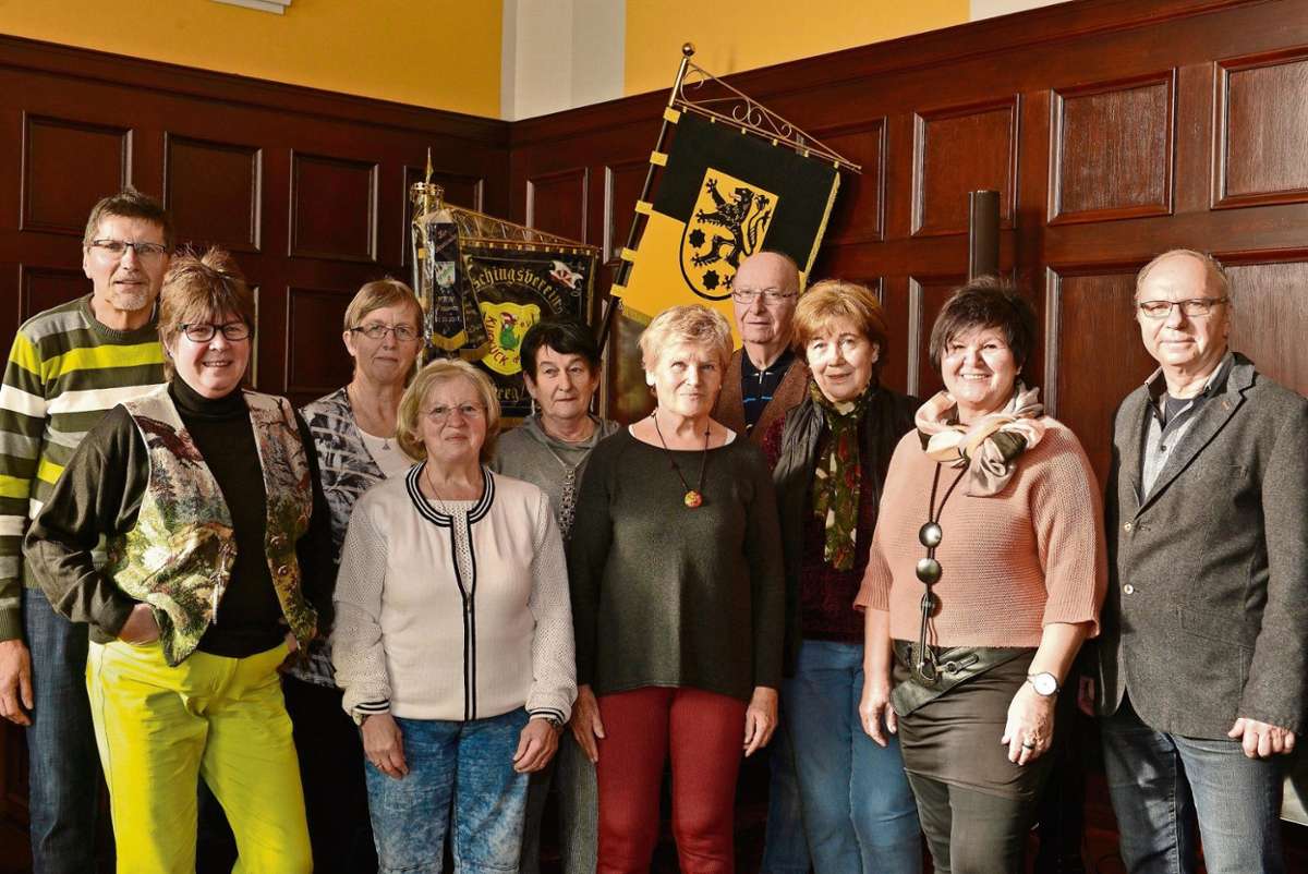 Eine Gruppe älterer Personen steht vor einer Holzwand.