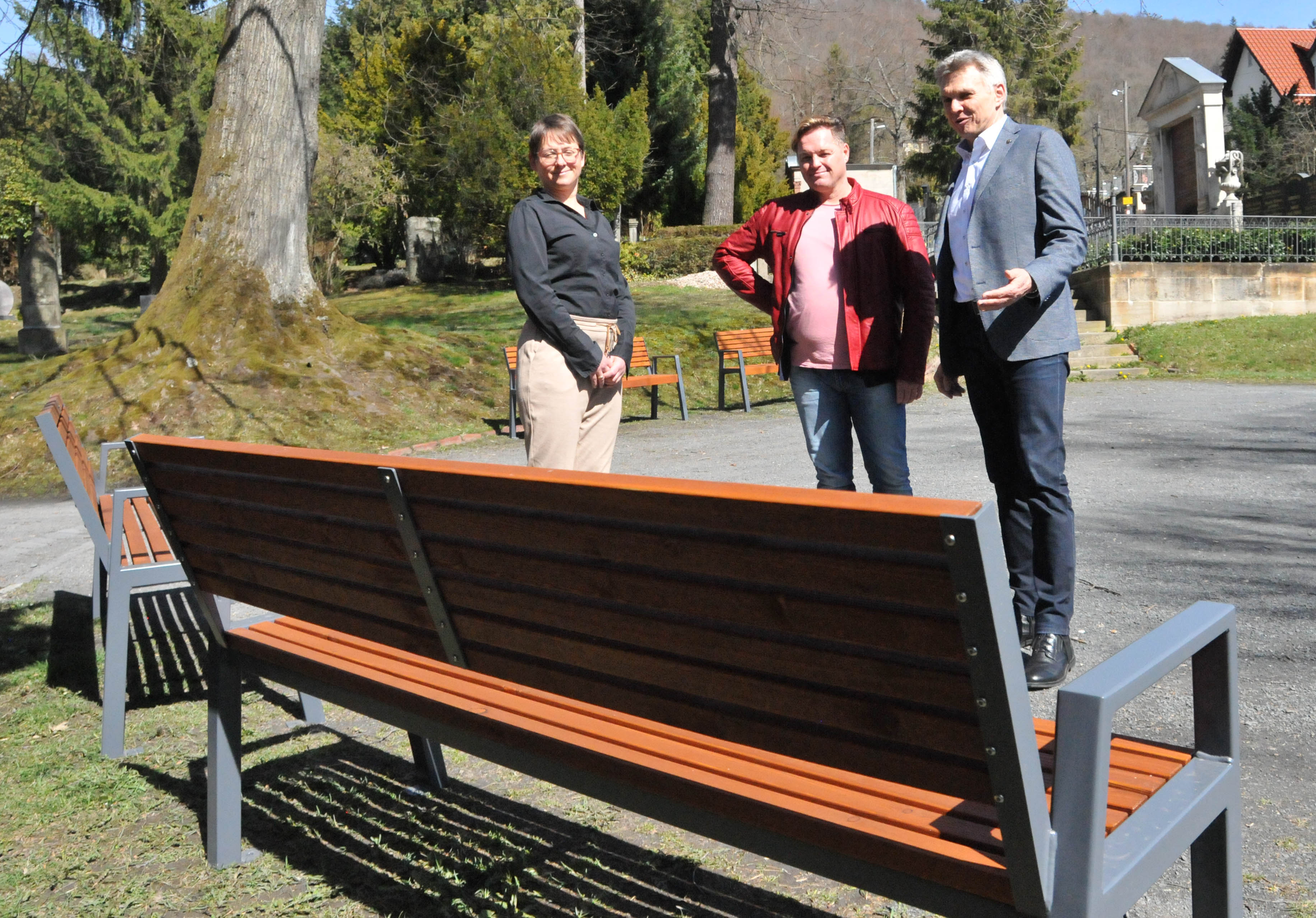 Drei Personen stehen draußen vor einer Bank und schauen diese an.