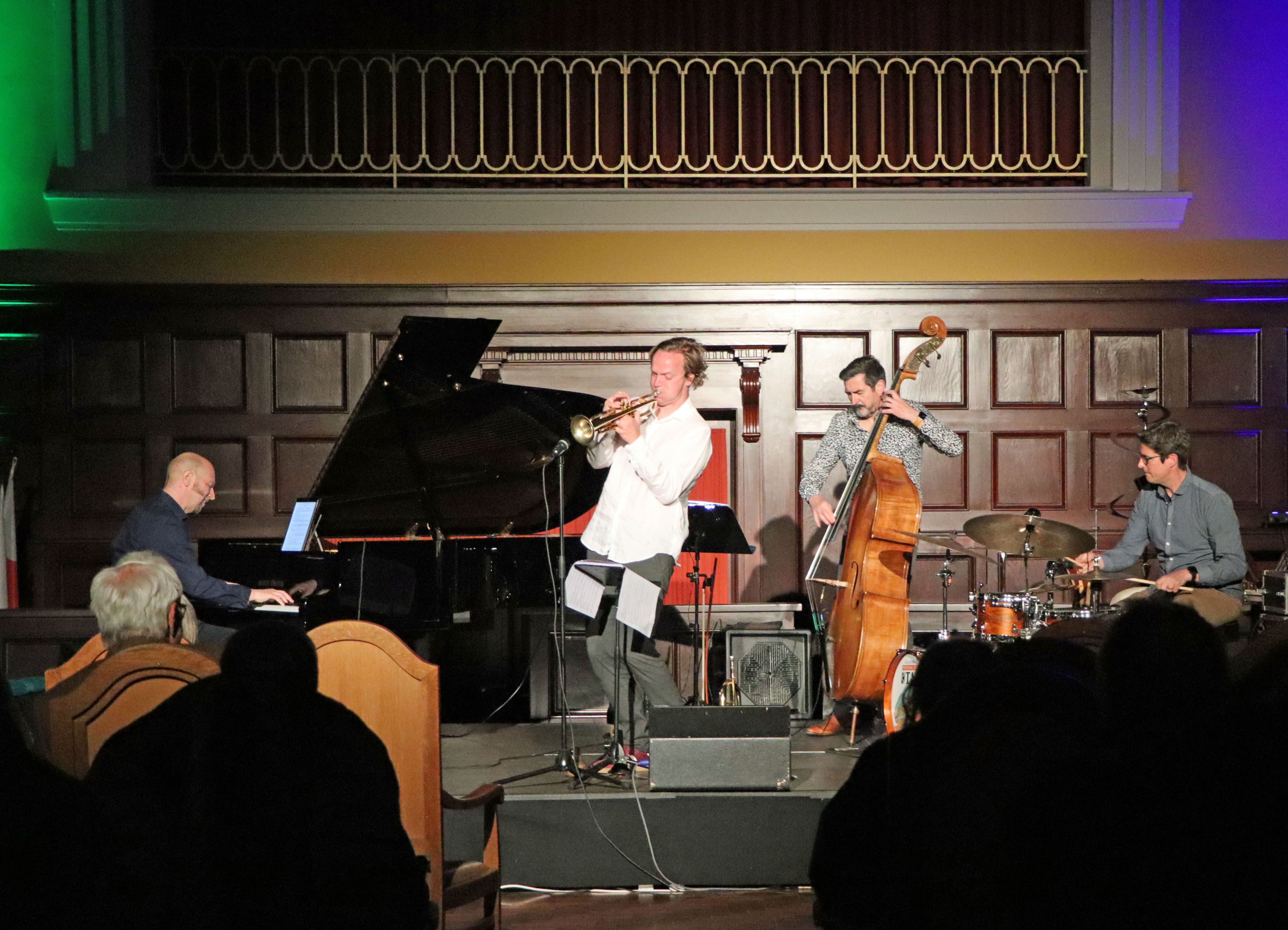 Eine Band steht mit ihren Intrumenten auf einer Bühne und spielt.