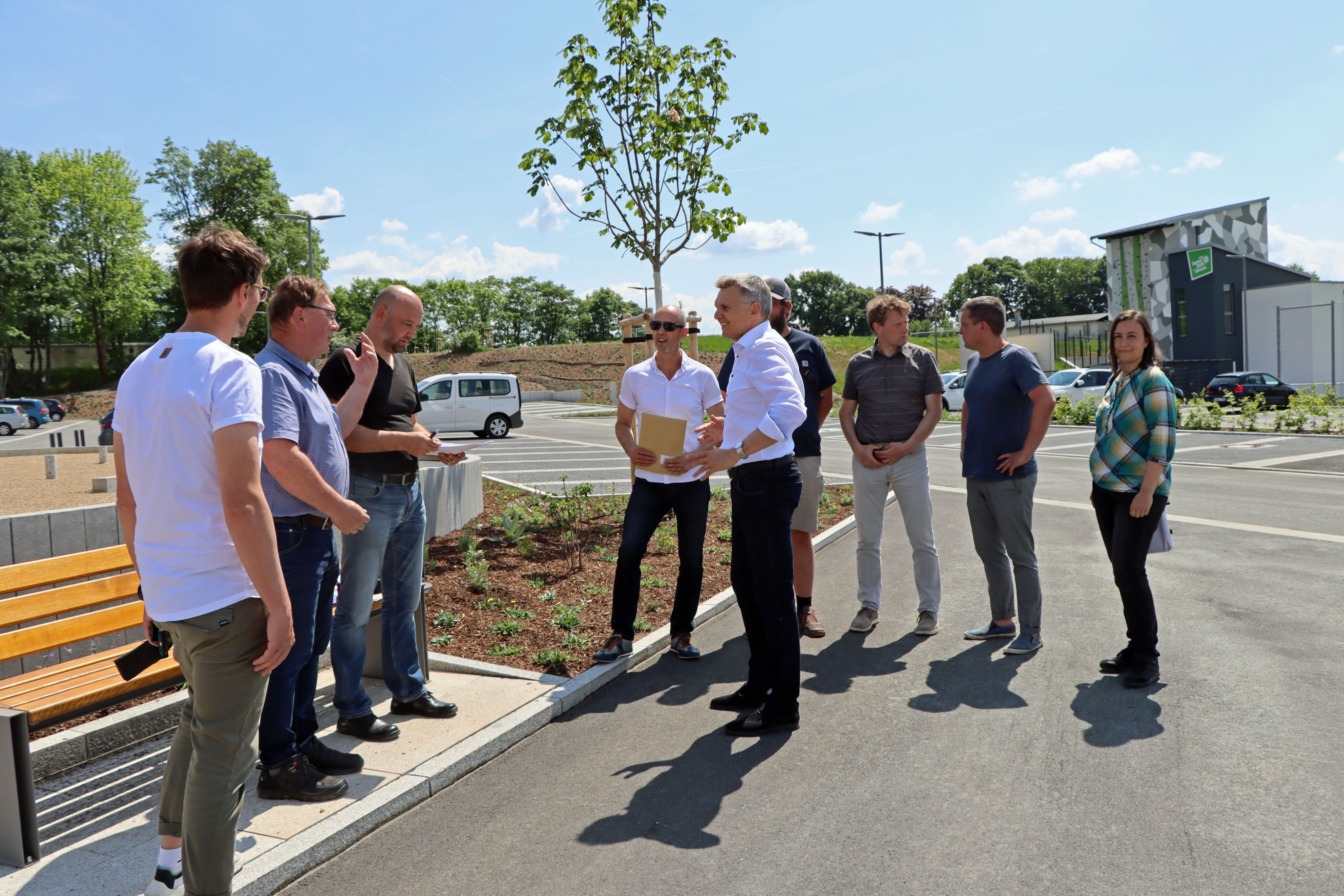 Mehrere Personen stehen auf einem Parkplatz. Die Sonne scheint.