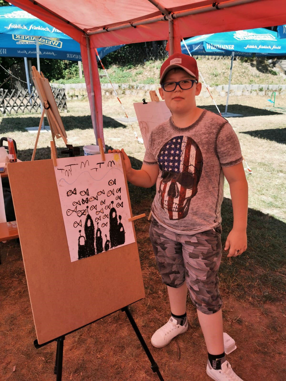 Ein Junge steht vor einer Staffelei und präsentiert sein Bild. Auf dem Bild sind Fische unter dem Wasser.
