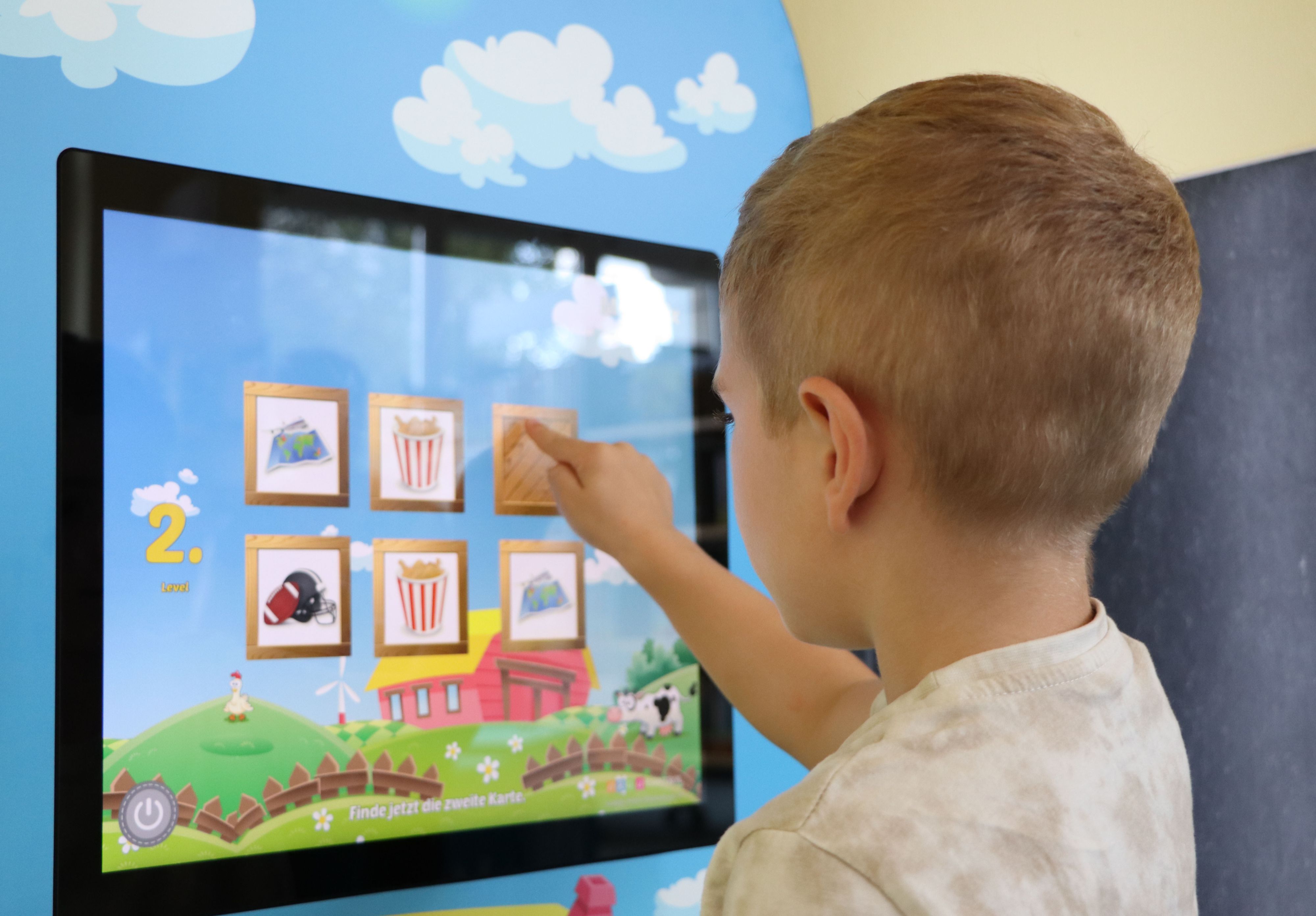Ein Kind tippt auf einen Bildschirm. Auf dem Bildschirm läuft ein Memory-Spiel.