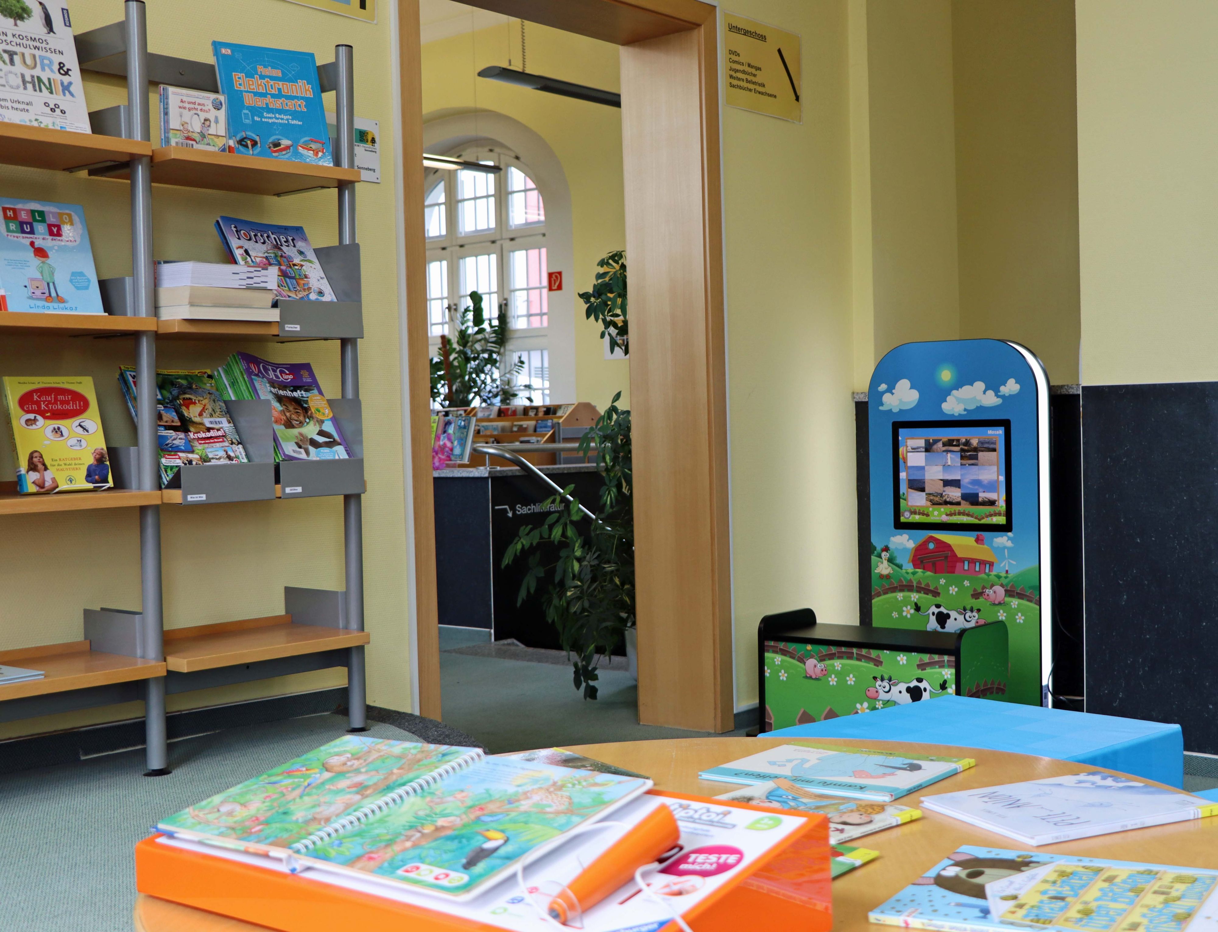 Im Vordergrund liegen Kinderbücher auf einem Tisch. Im Hintergrund steht ein Spielautomat mit Tieren darauf.