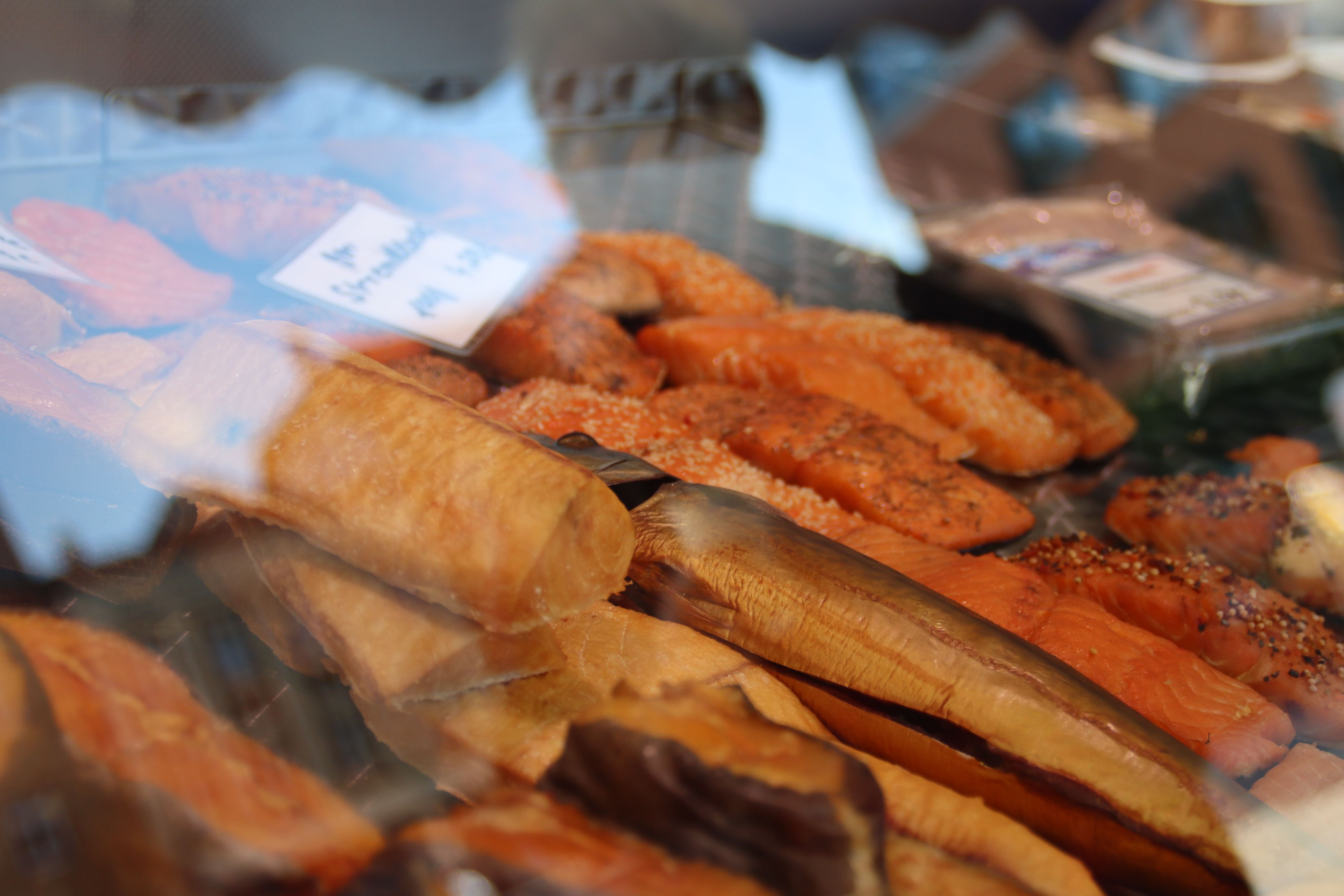 Hinter der Scheibe einer Verkaufstheke liegt frischer und geräucherter Fisch.