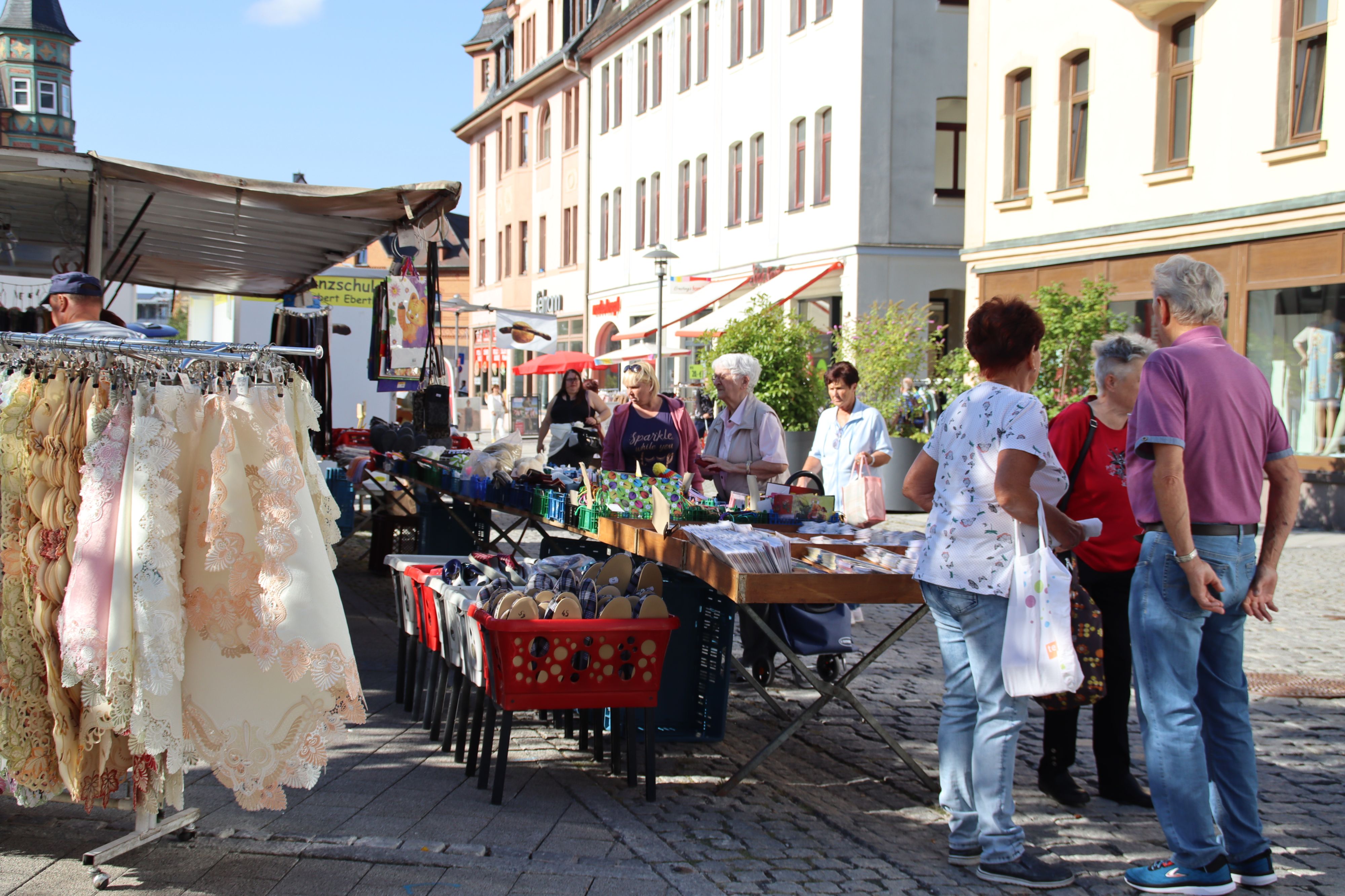 In der Fußgängerzone steht ein Verkaufsstand mit Textilien. Um den Stand herum stehen interessierte Kunden.