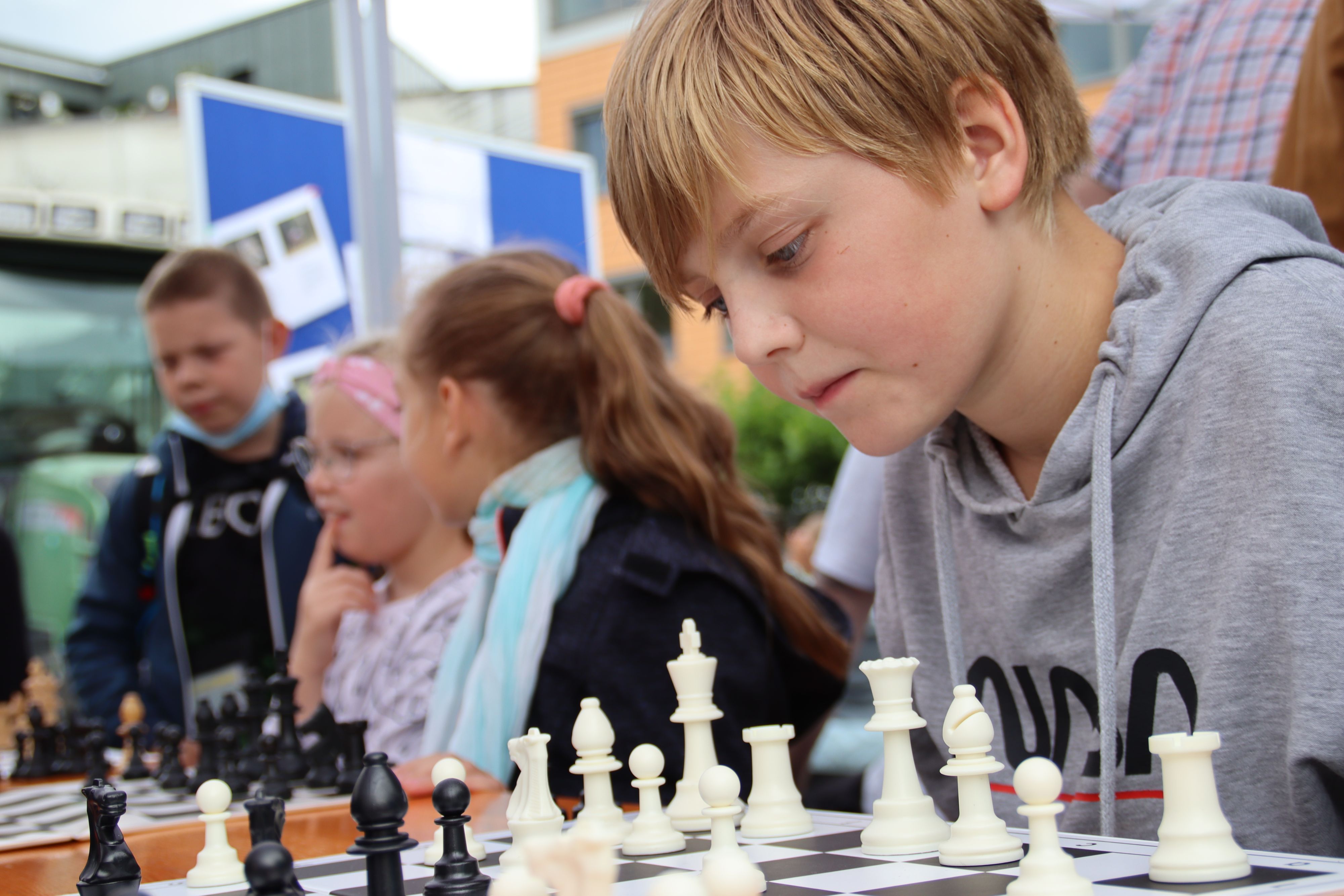 Kinder sitzen vor einem Schachbrett und spielen Schach.